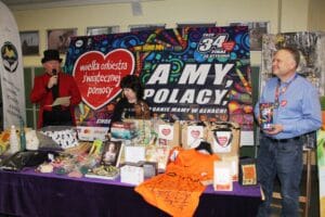 Stoisko szkolne z fantami przygotowanymi na finał Wielkiej Orkiestry Świątecznej Pomocy, z prowadzącymi prezentującymi przedmioty do licytacji