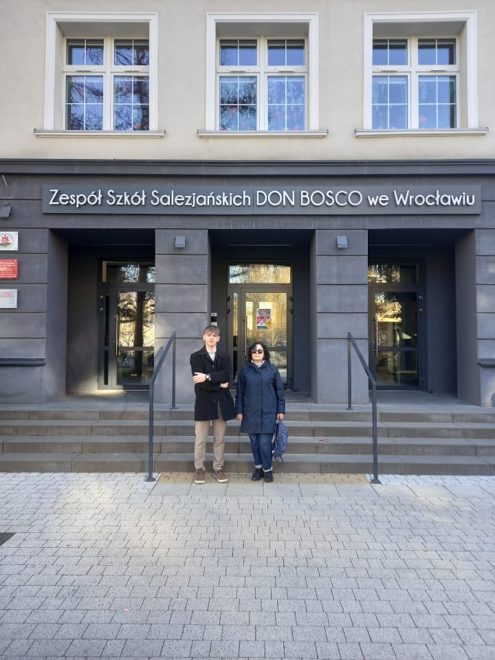 Logo Olimpiady Znajomości Afryki przedstawiające kontur kontynentu afrykańskiego podzielony na cztery barwne pola: żółte, czerwone, czarne i zielone. Pola rozdzielone są białym kształtem krzyża. Poniżej znajduje się napis: OLIMPIADA ZNAJOMOŚCI AFRYKI