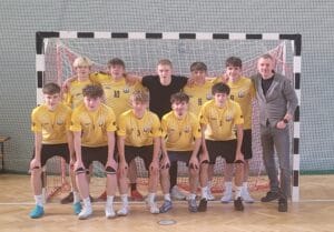 Oficjalne zdjęcie grupowe męskiej drużyny futsalu Zespołu Szkół nr 2 w Lubinie wraz z trenerem, pozujących w hali sportowej na tle bramki po zdobyciu tytułu Mistrza Dolnego Śląska. Zawodnicy są w żółto-białych strojach, a na szyjach mają medale.