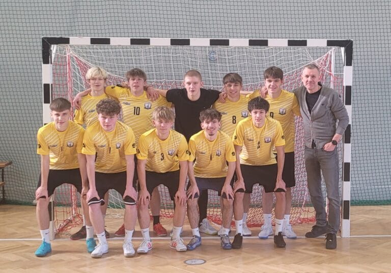 Oficjalne zdjęcie grupowe męskiej drużyny futsalu Zespołu Szkół nr 2 w Lubinie wraz z trenerem, pozujących w hali sportowej na tle bramki po zdobyciu tytułu Mistrza Dolnego Śląska. Zawodnicy są w żółto-białych strojach, a na szyjach mają medale.