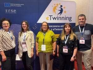 Grupa pięciu uczestników konferencji – trzech kobiet i dwóch mężczyzn – pozuje na tle ścianki reklamowej eTwinning z napisami FRSE i Dofinansowane przez Unię Europejską. Wszyscy mają identyfikatory na smyczach