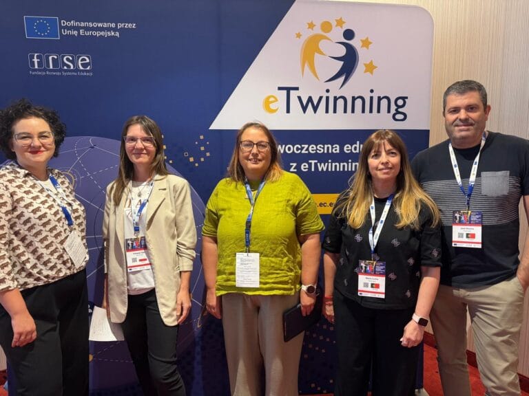 Grupa pięciu uczestników konferencji – trzech kobiet i dwóch mężczyzn – pozuje na tle ścianki reklamowej eTwinning z napisami FRSE i Dofinansowane przez Unię Europejską. Wszyscy mają identyfikatory na smyczach